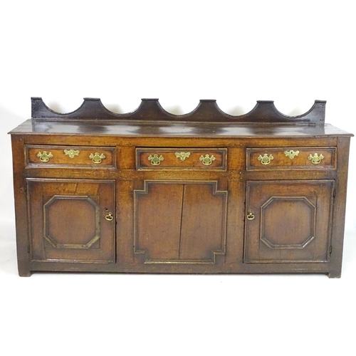 1393A - An 18thC oak dresser base with a shaped upstand above three short drawers with brass back plates and... 