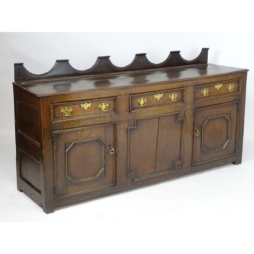 1393A - An 18thC oak dresser base with a shaped upstand above three short drawers with brass back plates and... 