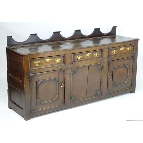 1393A - An 18thC oak dresser base with a shaped upstand above three short drawers with brass back plates and... 