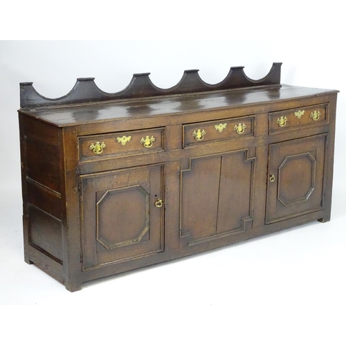 1393A - An 18thC oak dresser base with a shaped upstand above three short drawers with brass back plates and... 