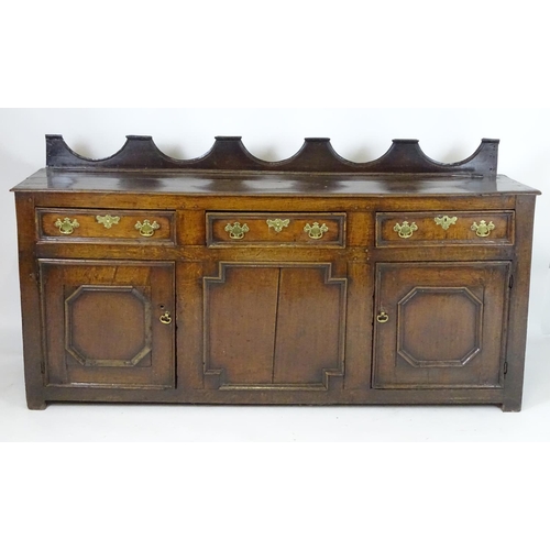 1393A - An 18thC oak dresser base with a shaped upstand above three short drawers with brass back plates and... 