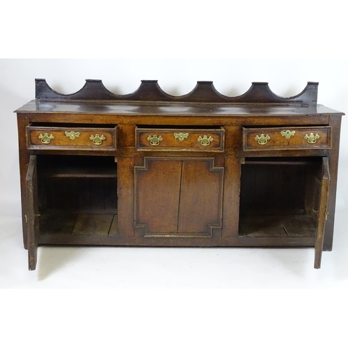 1393A - An 18thC oak dresser base with a shaped upstand above three short drawers with brass back plates and... 