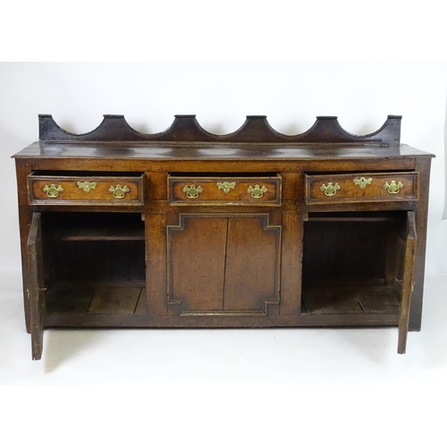 1393A - An 18thC oak dresser base with a shaped upstand above three short drawers with brass back plates and... 