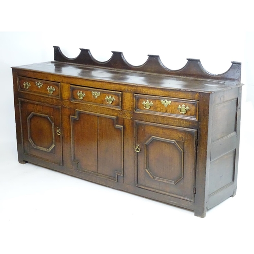 1393A - An 18thC oak dresser base with a shaped upstand above three short drawers with brass back plates and... 