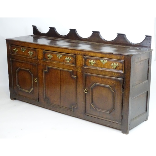 1393A - An 18thC oak dresser base with a shaped upstand above three short drawers with brass back plates and... 