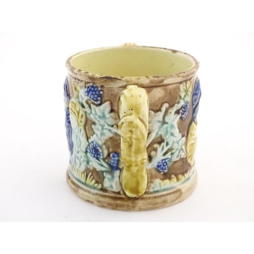 87 - A majolica loving cup / twin handled mug decorated with moulded figures in relief amongst vine leave... 