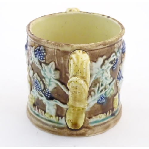 87 - A majolica loving cup / twin handled mug decorated with moulded figures in relief amongst vine leave... 