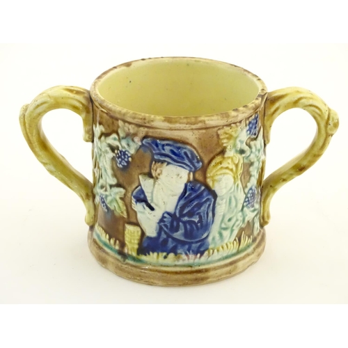 87 - A majolica loving cup / twin handled mug decorated with moulded figures in relief amongst vine leave... 