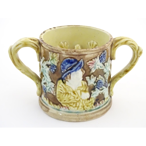 87 - A majolica loving cup / twin handled mug decorated with moulded figures in relief amongst vine leave... 