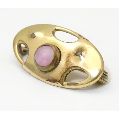 924 - An Arts & Crafts gilt metal brooch set with pink stone cabochon. Marked to reverse with monogram for... 