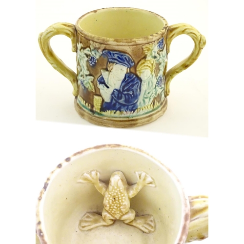 87 - A majolica loving cup / twin handled mug decorated with moulded figures in relief amongst vine leave... 