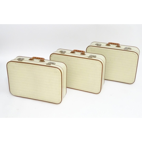 1341 - A mid 20thC set of three travelling suitcases by Cheney, London, in white with tan trim, each with d... 