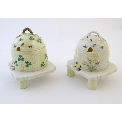 128 - Two Belleek honey / preserve pots and covers formed as bee hives / skeps with bee, shamrock / cover ... 