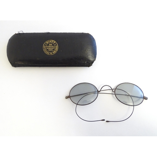 1289 - A cased pair of early 20thC spectacles / glasses with a steel frame, tinted oval lenses and flexible... 