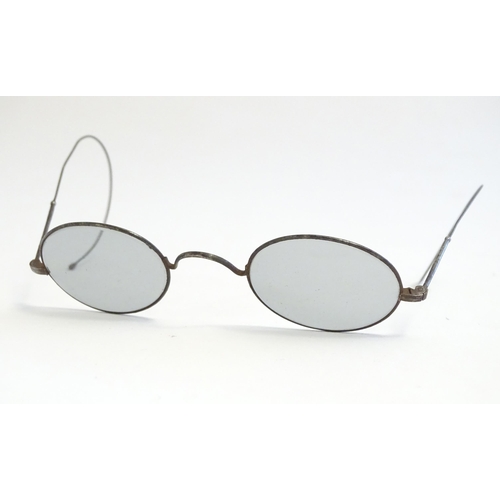 1289 - A cased pair of early 20thC spectacles / glasses with a steel frame, tinted oval lenses and flexible... 