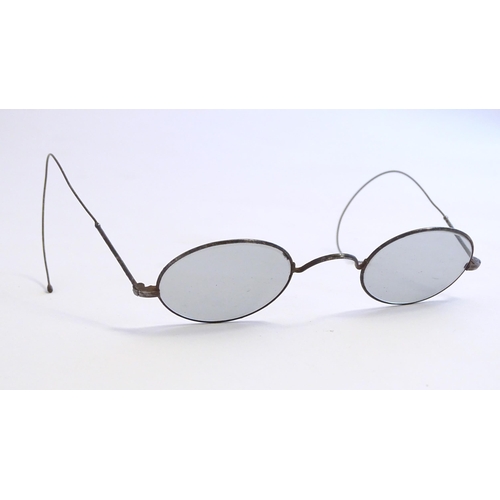 1289 - A cased pair of early 20thC spectacles / glasses with a steel frame, tinted oval lenses and flexible... 