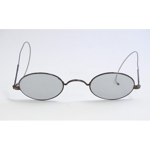 1289 - A cased pair of early 20thC spectacles / glasses with a steel frame, tinted oval lenses and flexible... 