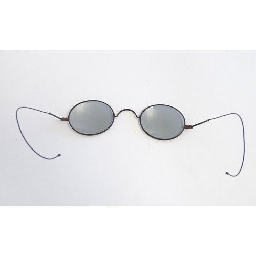 1289 - A cased pair of early 20thC spectacles / glasses with a steel frame, tinted oval lenses and flexible... 