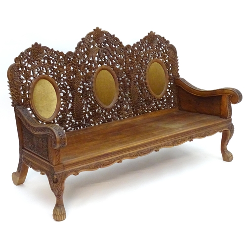 2204 - A carved oriental sofa with pierced decoration and three backrests above swept arms, a panelled seat... 