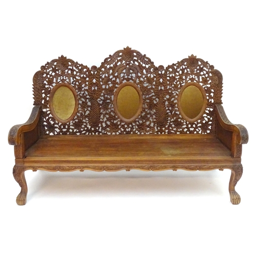 2204 - A carved oriental sofa with pierced decoration and three backrests above swept arms, a panelled seat... 