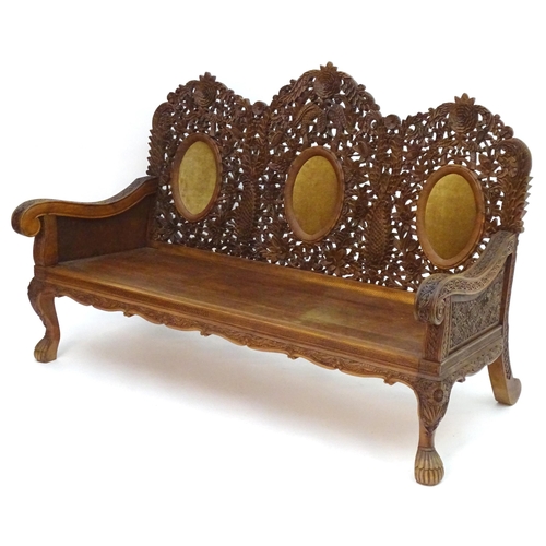 2204 - A carved oriental sofa with pierced decoration and three backrests above swept arms, a panelled seat... 