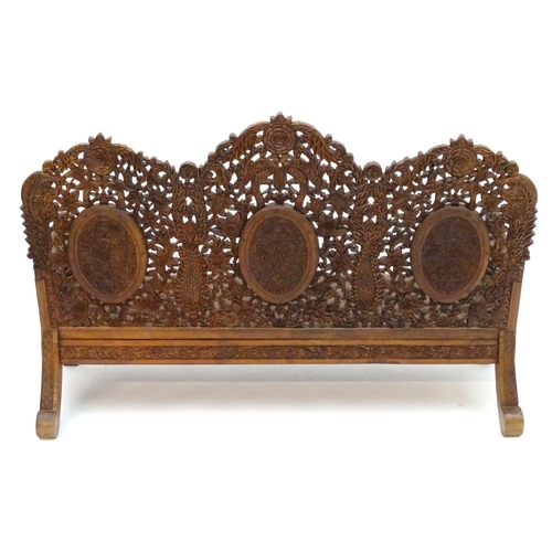 2204 - A carved oriental sofa with pierced decoration and three backrests above swept arms, a panelled seat... 