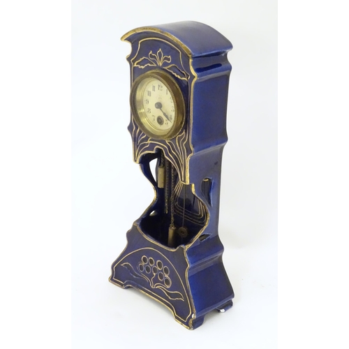 2286 - A Jugendstil mantle clock formed as a ceramic cased long case clock with blue and gilt detail. the d... 