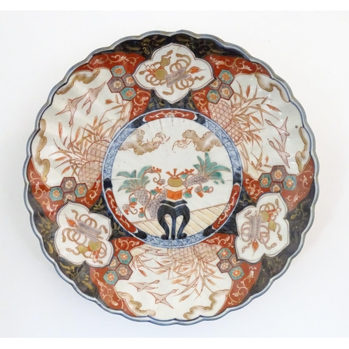37 - An Oriental charger with scalloped edge in the Imari palette decorated with a stylised censor on sta... 