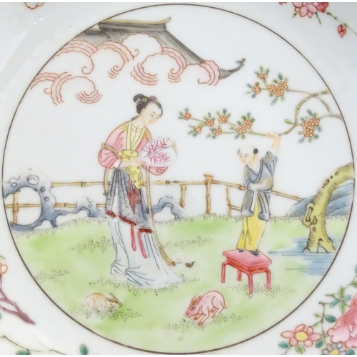 37 - A Chinese famille rose plate decorated with a woman holding a fan in a garden terrace with a young a... 
