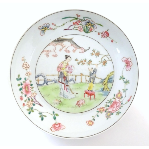 20 - A Chinese famille rose plate decorated with a woman holding a fan in a garden terrace with a young a... 