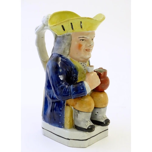 86A - A Toby jug modelled as a seated man holding a beaker and a jug, with moulded caryatid handle. Approx... 