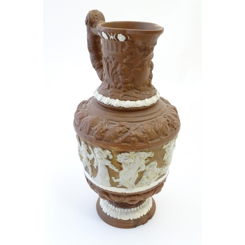 185 - A large Continental pottery jug with moulded decoration and rams head handle. The body decorated wit... 