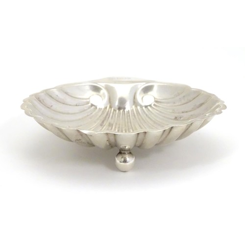 358 - A silver scallop-shaped dish raised on three bun feet. Hallmarked Sheffield 1910 maker Harrison Brot... 