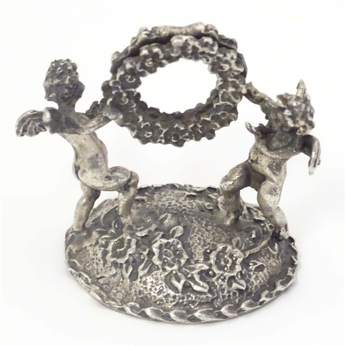 489 - A Continental white metal table / place card holder formed as cherubs/ cupids holding a flower garla... 