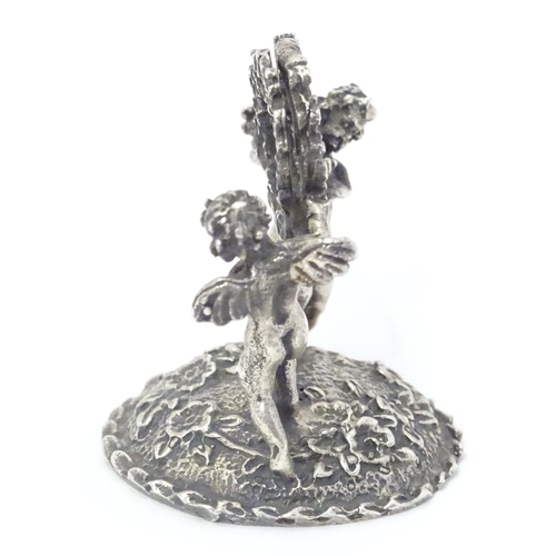 489 - A Continental white metal table / place card holder formed as cherubs/ cupids holding a flower garla... 