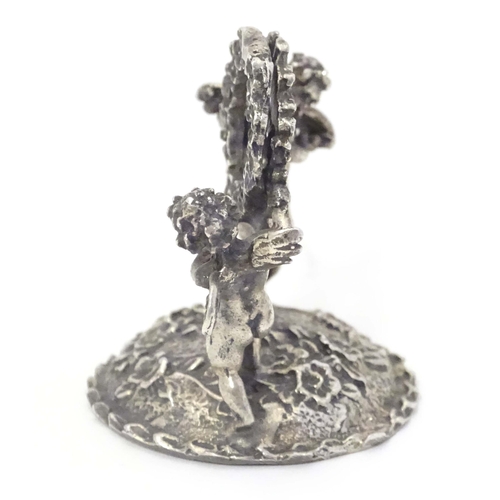 489 - A Continental white metal table / place card holder formed as cherubs/ cupids holding a flower garla... 