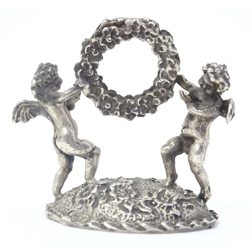 489 - A Continental white metal table / place card holder formed as cherubs/ cupids holding a flower garla... 