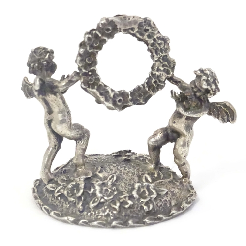 489 - A Continental white metal table / place card holder formed as cherubs/ cupids holding a flower garla... 