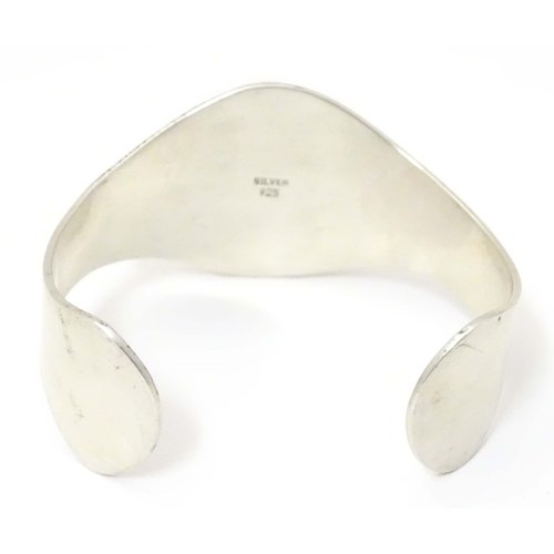 711 - A .925 silver bracelet of cuff bangle form with shiva shell decoration.