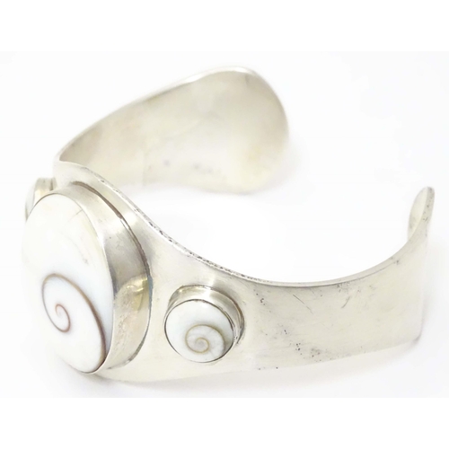 711 - A .925 silver bracelet of cuff bangle form with shiva shell decoration.