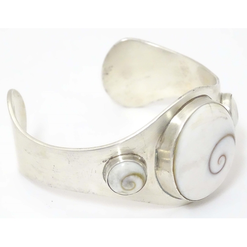 711 - A .925 silver bracelet of cuff bangle form with shiva shell decoration.