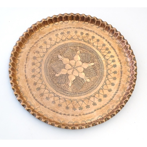 998 - An early 20thC copper charger with scalloped edge, central Arts & Crafts style floral motif and band... 