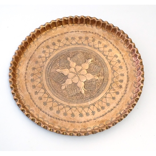 998 - An early 20thC copper charger with scalloped edge, central Arts & Crafts style floral motif and band... 