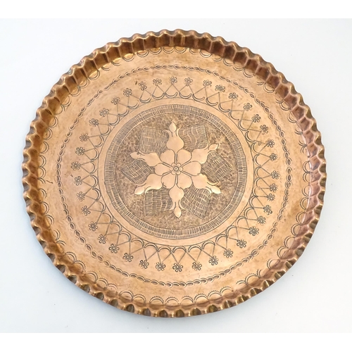 998 - An early 20thC copper charger with scalloped edge, central Arts & Crafts style floral motif and band... 