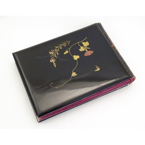 1054 - A Japanese photograph album with lacquered boards, the cover decorated with figures travelling by ha... 