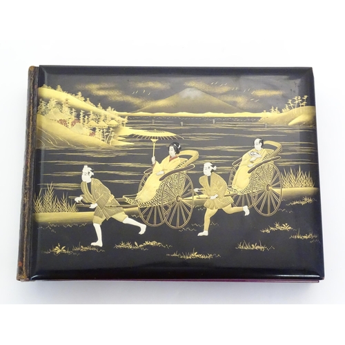 1054 - A Japanese photograph album with lacquered boards, the cover decorated with figures travelling by ha... 