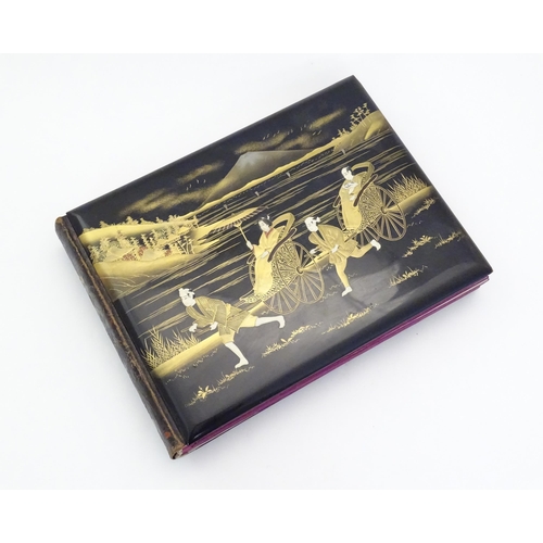 1054 - A Japanese photograph album with lacquered boards, the cover decorated with figures travelling by ha... 