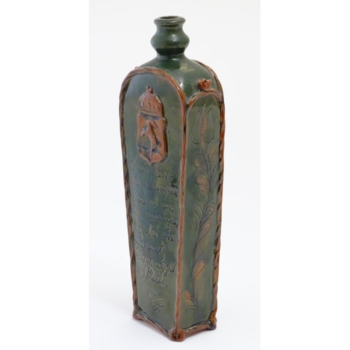 1096 - A Continental terracotta gin / spirit bottle / flask of tapering form with a green glaze, incised sc... 