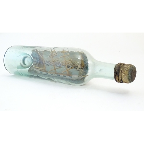 1129 - A 20thC scratch built ship in bottle with postcard backdrop depicting a waterfront with boats and bu... 