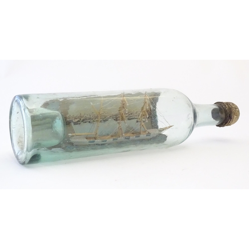 1129 - A 20thC scratch built ship in bottle with postcard backdrop depicting a waterfront with boats and bu... 